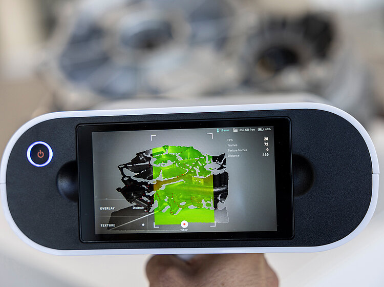 Handgehaltenes digitales Messgerät mit Bildschirm, der eine 3D-Scanansicht eines Objekts in grünen, schwarzen und weißen Farben anzeigt.