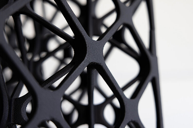 Nahaufnahme eines modernen schwarzen Gitters aus Metall mit geometrischem Muster und glatter Oberfläche vor weißem Hintergrund.