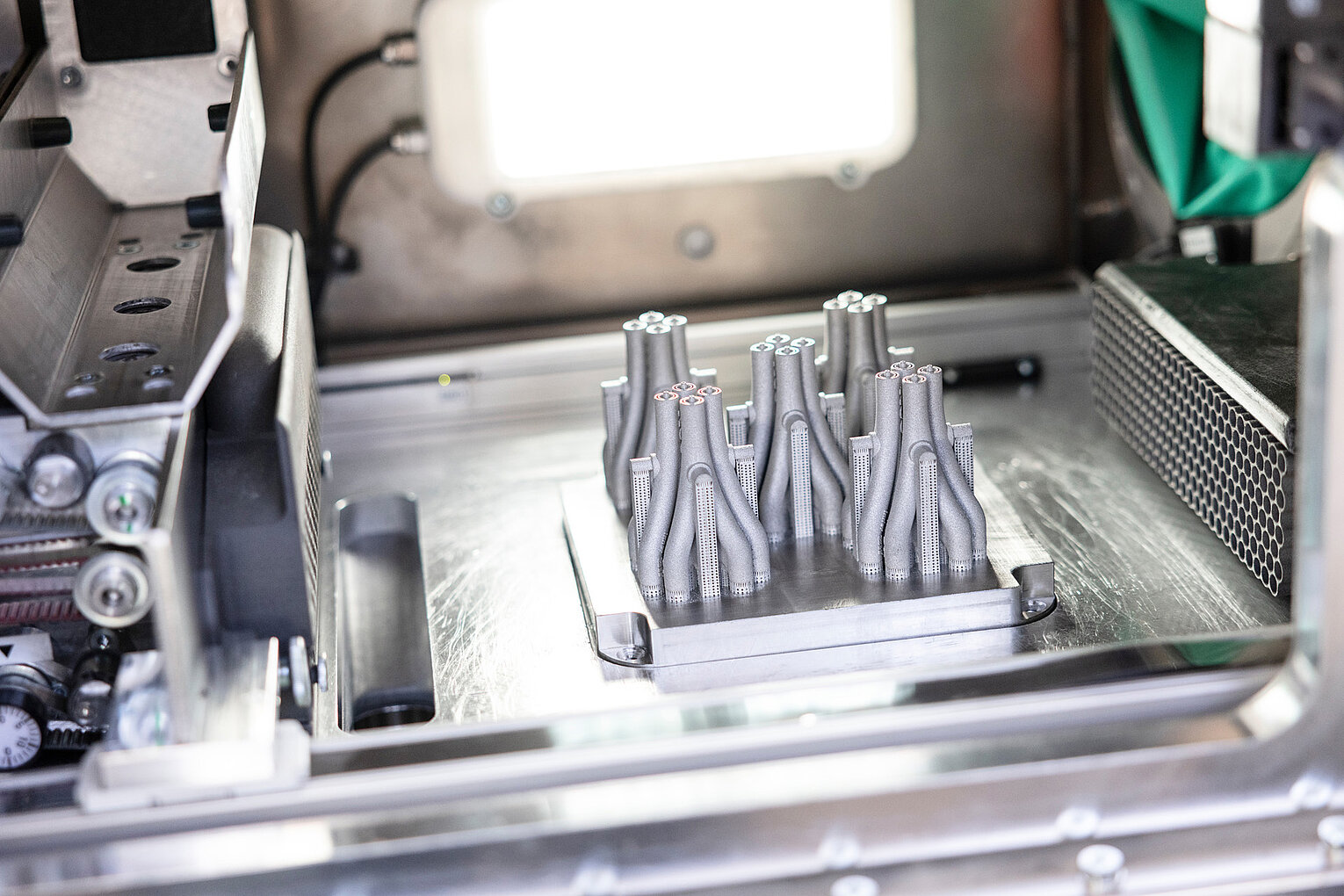 3D-gedruckte Bauteile aus Metall in einer industriellen 3D-Druckmaschine auf einer Metallplatte.