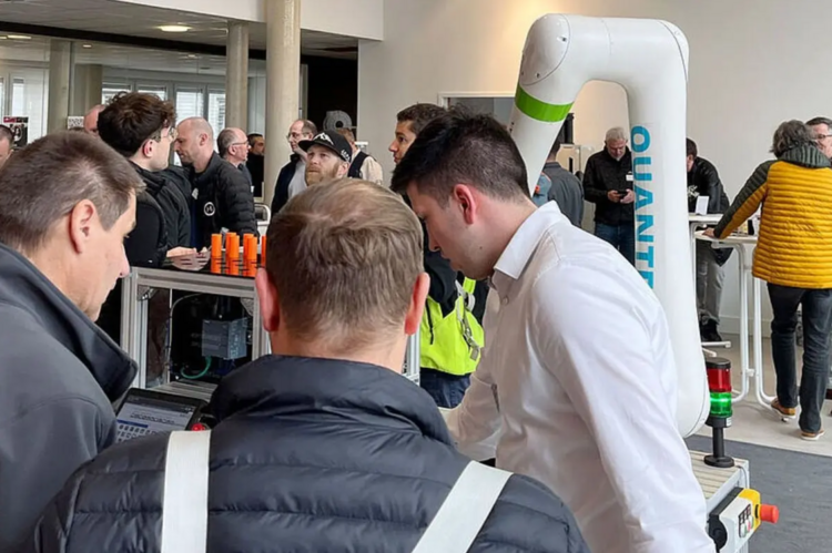 Menschen stehen in einem Raum und betrachten eine Demonstration eines Roboterarms mit der Aufschrift Quantum.