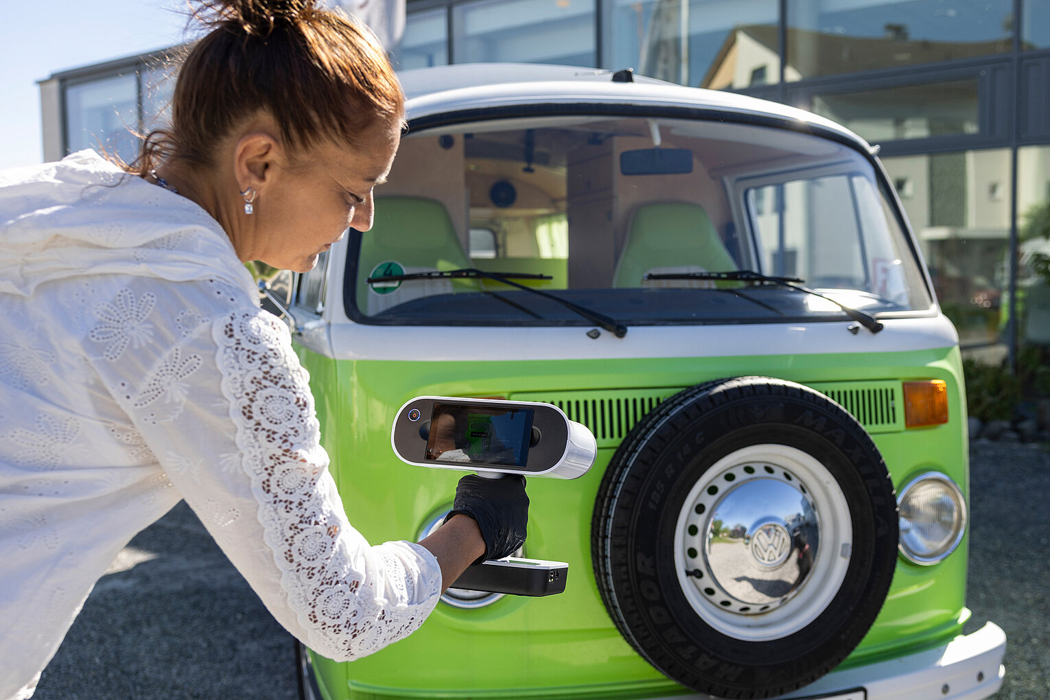 Frau lädt ein Elektroauto an der Vorderseite auf einem sonnigen Parkplatz auf.