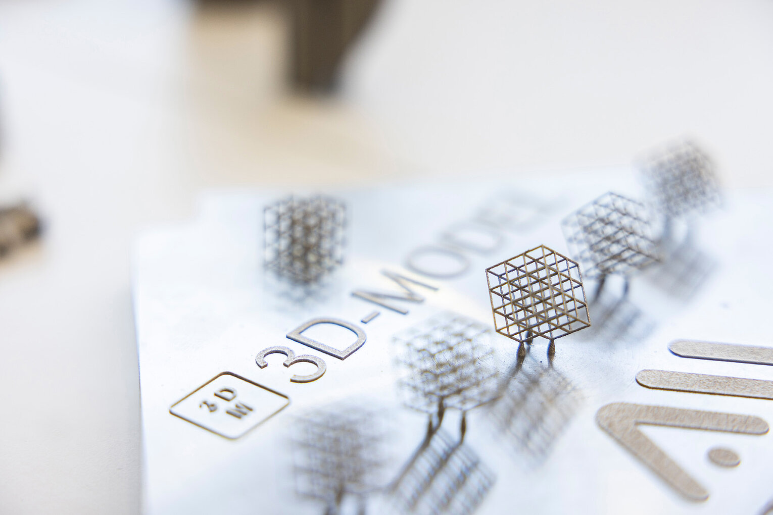 Mehrere kleine, fein strukturierte 3D-gedruckte Modelle in Form von Würfeln mit offener Gitterstruktur stehen auf einem weißen Blatt mit der Aufschrift 3D-MODEL.