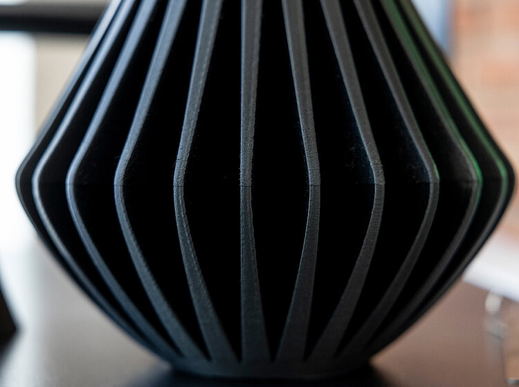 Nahaufnahme einer schwarzen Vase mit vertikalen, gleichmäßigen Rippen, die eine geometrische, modernistische Form ergeben.